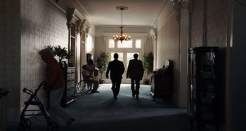 Movie still from “Bad Lieutenant: Port of Call New Orleans” (2009), directed by Werner Herzog – Two men are walking down the hall of a house; Wide shot, Low angle