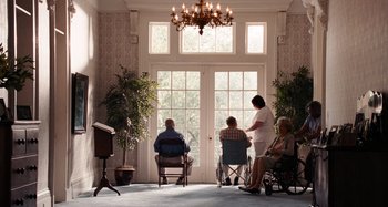 Movie still from “Bad Lieutenant: Port of Call New Orleans” (2009), directed by Werner Herzog – A group of people sitting in chairs in front of a window; Wide shot, Low angle