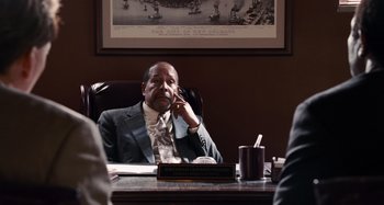 Movie still from “Bad Lieutenant: Port of Call New Orleans” (2009), directed by Werner Herzog – A man sitting at a desk talking on a phone; Medium shot, Over the shoulder angle