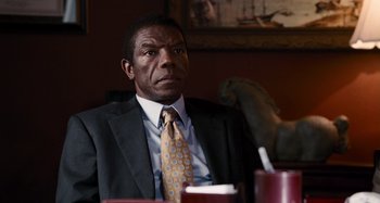 Movie still from “Bad Lieutenant: Port of Call New Orleans” (2009), directed by Werner Herzog – A man sitting at a table in a suit and tie; Medium shot, Over the shoulder angle