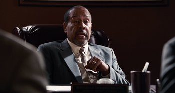 Movie still from “Bad Lieutenant: Port of Call New Orleans” (2009), directed by Werner Herzog – A man in a suit and tie sitting at a table; Medium shot, Over the shoulder angle