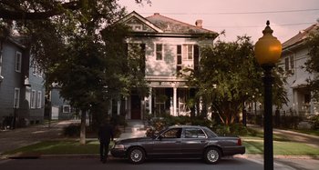 Movie still from “Bad Lieutenant: Port of Call New Orleans” (2009), directed by Werner Herzog – A man standing next to a car parked in front of a house; Extreme Wide shot, Low angle