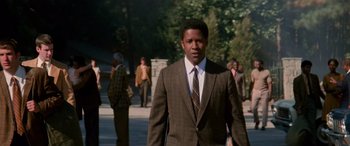 Movie still from “Remember the Titans” (2000), directed by Boaz Yakin – A man wearing a suit and tie walking down a street; Medium shot, Low angle
