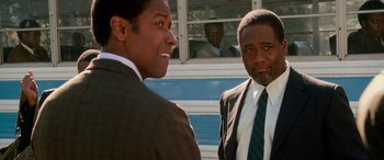 Movie still from “Remember the Titans” (2000), directed by Boaz Yakin – Two men in suits standing next to each other in front of a bus; Close Up shot, Over the shoulder angle