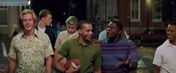 Movie still from “Remember the Titans” (2000), directed by Boaz Yakin – A group of men standing next to each other holding a football; Medium shot, Low angle