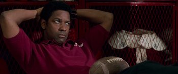 Movie still from “Remember the Titans” (2000), directed by Boaz Yakin – A man sitting in front of a fence holding a football; Close Up shot, High angle