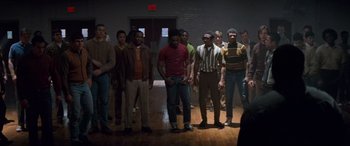 Movie still from “Remember the Titans” (2000), directed by Boaz Yakin – A group of men standing next to each other in a room; Wide shot, High angle