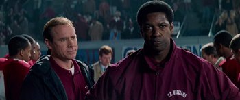 Movie still from “Remember the Titans” (2000), directed by Boaz Yakin – Two men standing next to each other in front of a crowd of onlookers; Close Up shot, Over the shoulder angle