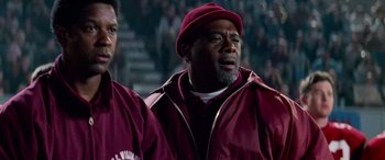Movie still from “Remember the Titans” (2000), directed by Boaz Yakin – A man in a maroon jacket and a red hat is standing in front of a crowd; Close Up shot, Low angle