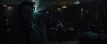 Movie still from “Reminiscence” (2021), directed by Lisa Joy – A group of people sitting at a table in a dark room; Medium shot, Over the shoulder angle