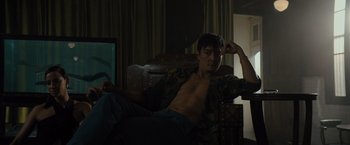 Movie still from “Reminiscence” (2021), directed by Lisa Joy – A shirtless man sitting in a chair in a dark room; Medium shot, Low angle