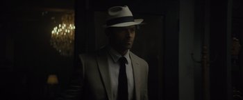 Movie still from “Reminiscence” (2021), directed by Lisa Joy – A man in a suit and hat standing in a dark room; Close Up shot, Over the shoulder angle
