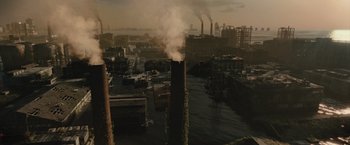 Movie still from “Reminiscence” (2021), directed by Lisa Joy – Smoke billows out of a factory chimney in an industrial setting; Extreme Wide shot, High angle