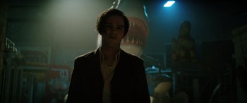 Movie still from “Renfield” (2023), directed by Chris McKay – A man standing in a dark room with a shark in the background; Close Up shot, Low angle