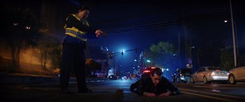Movie still from “Renfield” (2023), directed by Chris McKay – A police officer standing next to a man laying on the ground; Wide shot, High angle