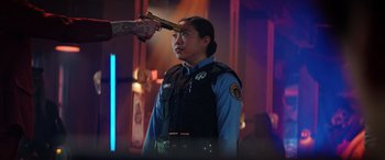 Movie still from “Renfield” (2023), directed by Chris McKay – A police officer with a gun pointed at his head; Medium shot, Over the shoulder angle