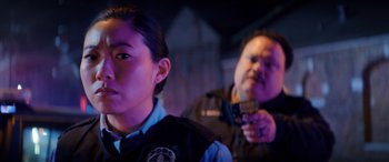 Movie still from “Renfield” (2023), directed by Chris McKay – A man and a woman in police uniforms with guns in their hands; Close Up shot, Over the shoulder angle