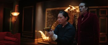 Movie still from “Renfield” (2023), directed by Chris McKay – A person holding a gun in a room with a fire place; Medium shot, Over the shoulder angle