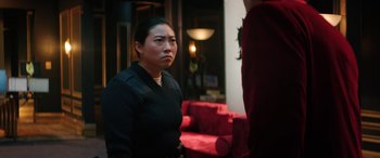 Movie still from “Renfield” (2023), directed by Chris McKay – A woman in a black shirt is sitting on a red couch; Medium shot, Over the shoulder angle