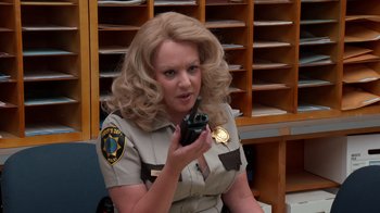 Movie still from “Reno 911!: The Hunt for QAnon” (2021), directed by Robert Ben Garant – A woman holding a cell phone while wearing a uniform; Close Up shot, High angle