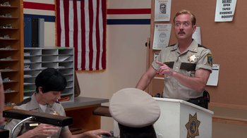 Movie still from “Reno 911!: The Hunt for QAnon” (2021), directed by Robert Ben Garant – A man in a police uniform talking to a man in a hat; Medium shot, Over the shoulder angle