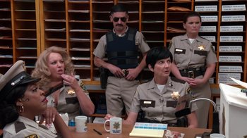 Movie still from “Reno 911!: The Hunt for QAnon” (2021), directed by Robert Ben Garant – A group of police officers sitting at a table; Medium shot, Over the shoulder angle