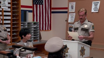 Movie still from “Reno 911!: The Hunt for QAnon” (2021), directed by Robert Ben Garant – A man in a police uniform standing in front of a woman; Medium shot, Over the shoulder angle