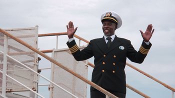 Movie still from “Reno 911!: The Hunt for QAnon” (2021), directed by Robert Ben Garant – A man in a suit and a hat waving; Medium shot, Low angle