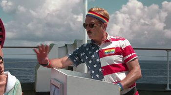 Movie still from “Reno 911!: The Hunt for QAnon” (2021), directed by Robert Ben Garant – A man wearing a patriotic shirt and a rainbow bracelet; Medium shot, Low angle