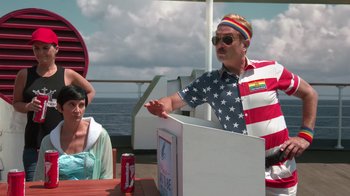 Movie still from “Reno 911!: The Hunt for QAnon” (2021), directed by Robert Ben Garant – A man wearing an american flag t - shirt is sitting in front of a woman; Medium shot, Over the shoulder angle