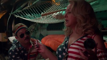 Movie still from “Reno 911!: The Hunt for QAnon” (2021), directed by Robert Ben Garant – A woman in american flag shirt looking at a cell phone; Medium shot, Over the shoulder angle