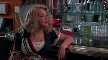 Movie still from “Reno 911!: The Hunt for QAnon” (2021), directed by Robert Ben Garant – A woman sitting at a bar with a glass of wine; Medium shot, Over the shoulder angle