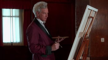 Movie still from “Reno 911!: The Hunt for QAnon” (2021), directed by Robert Ben Garant – A man in a robe holding a paintbrush and a palette; Medium shot, Over the shoulder angle