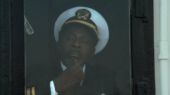 Movie still from “Reno 911!: The Hunt for QAnon” (2021), directed by Robert Ben Garant – A man wearing a hat and a suit looking out of a window; Close Up shot, High angle