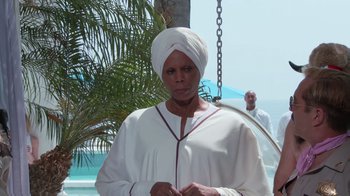 Movie still from “Reno 911!: The Hunt for QAnon” (2021), directed by Robert Ben Garant – An older woman wearing a turban and a white robe; Medium shot, Low angle