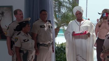 Movie still from “Reno 911!: The Hunt for QAnon” (2021), directed by Robert Ben Garant – A woman in a white robe is holding a red object; Medium shot, Low angle