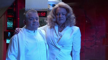 Movie still from “Reno 911!: The Hunt for QAnon” (2021), directed by Robert Ben Garant – A man and a woman standing next to each other; Medium shot, Low angle