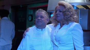 Movie still from “Reno 911!: The Hunt for QAnon” (2021), directed by Robert Ben Garant – A man and a woman posing for a picture; Medium shot, Over the shoulder angle