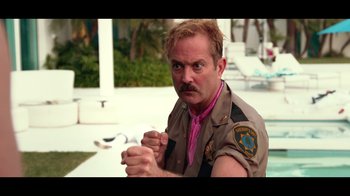 Movie still from “Reno 911!: The Hunt for QAnon” (2021), directed by Robert Ben Garant – A man with a mustache wearing a pink shirt and a pink tie; Medium shot, Over the shoulder angle