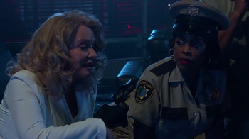Movie still from “Reno 911!: The Hunt for QAnon” (2021), directed by Robert Ben Garant – Two women are sitting next to each other in a dark room; Medium shot, Over the shoulder angle