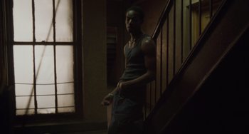 Movie still from “Requiem for a Dream” (2000), directed by Darren Aronofsky – A man standing on the stairs in a dark room; Medium shot, Low angle
