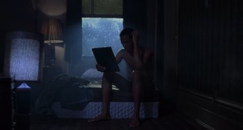 Movie still from “Requiem for a Dream” (2000), directed by Darren Aronofsky – A man sitting on a bed looking at a computer; Medium shot, Low angle