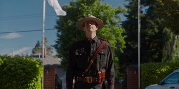 Movie still from “Rescued by Ruby” (2022), directed by Katt Shea – A man in a uniform and a hat is standing in front of a tree; Medium shot, Low angle