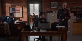 Movie still from “Rescued by Ruby” (2022), directed by Katt Shea – A man sitting in front of a laptop computer on top of a desk; Wide shot, Over the shoulder angle