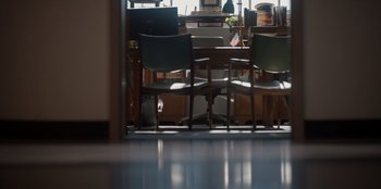 Movie still from “Rescued by Ruby” (2022), directed by Katt Shea – Two chairs are in front of a desk; Wide shot, High angle