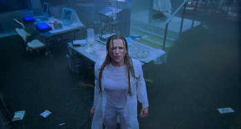 Movie still from “Resident Evil” (2002), directed by Paul W.S. Anderson – A woman standing in a room with a table; Medium shot, Low angle