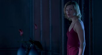 Movie still from “Resident Evil” (2002), directed by Paul W.S. Anderson – A woman in a red dress standing next to a window; Medium shot, Low angle