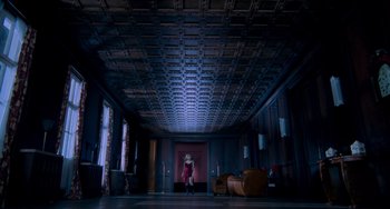 Movie still from “Resident Evil” (2002), directed by Paul W.S. Anderson – A woman standing in a dark room with a couch and chair; Extreme Wide shot, Low angle