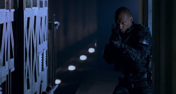 Movie still from “Resident Evil” (2002), directed by Paul W.S. Anderson – A man holding a gun while standing next to a wall; Medium shot, Low angle