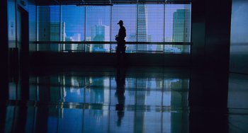 Movie still from “Resident Evil” (2002), directed by Paul W.S. Anderson – A man standing in front of a large window with a view of a city; Wide shot, Low angle
